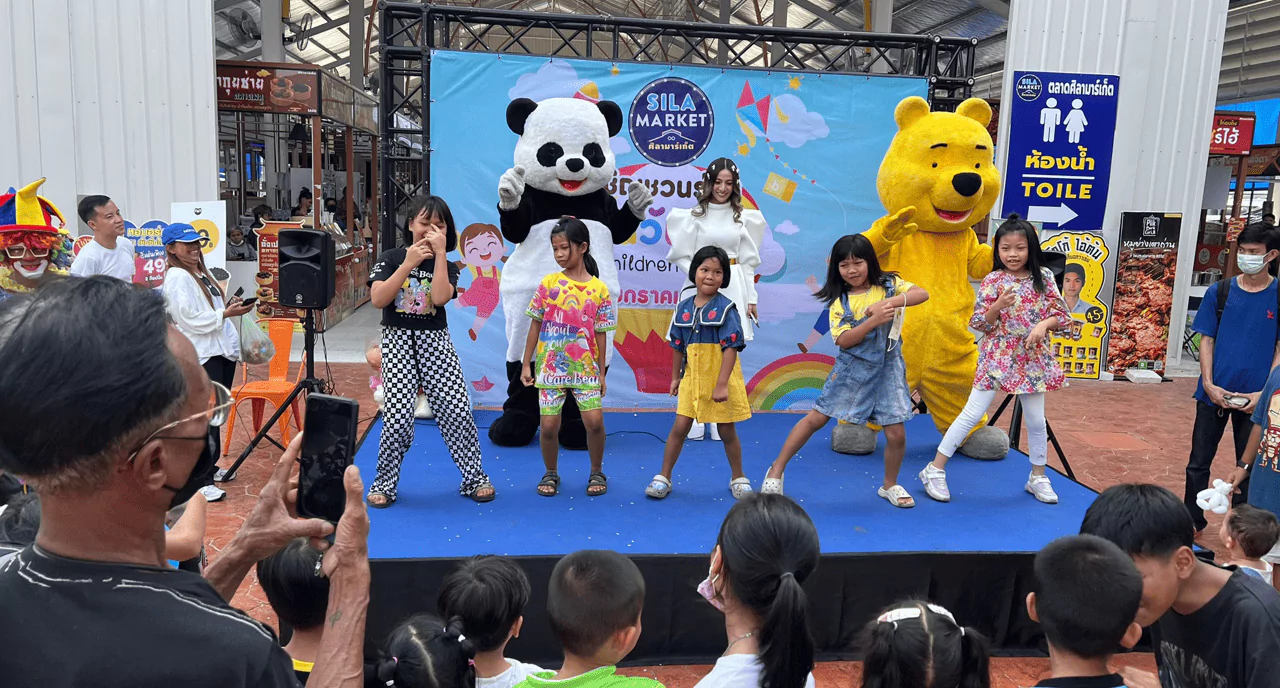 มาสคอสหมีแพนด้า มาสคอสหมีสีเหลือง และเด็กผู้หญิงหลายคนกำลังเต้นอยู่บนเวที