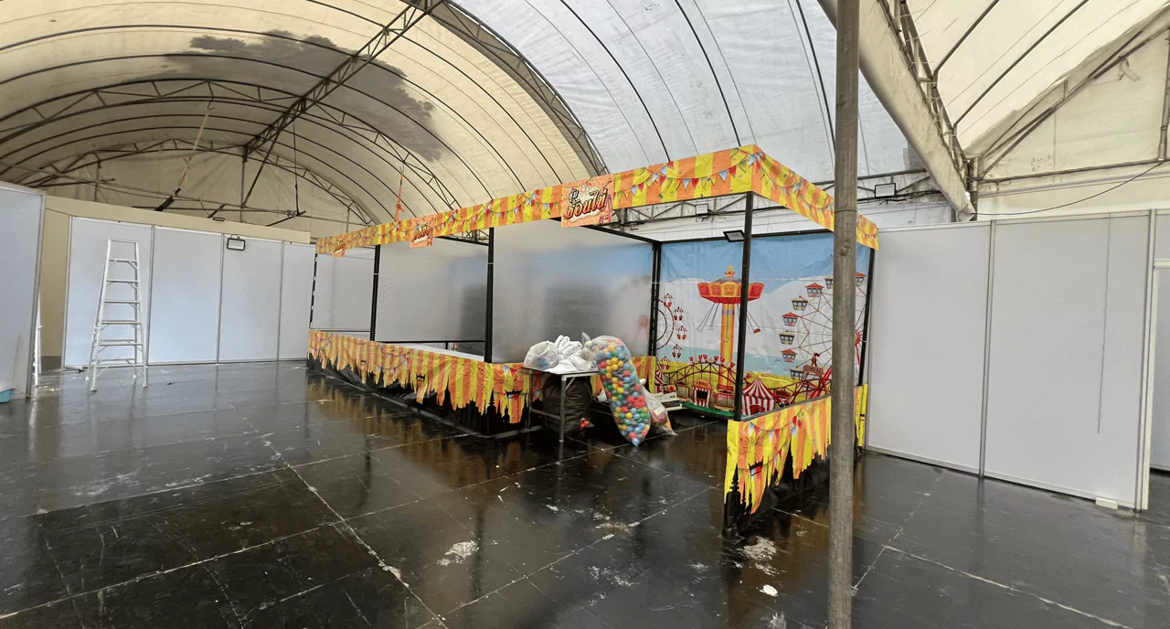 บูธกิจกรรมในร่มมีป้ายแบคดรอปข้างหลัง มีเต็นท์ผ้าใบสูงสีขาว