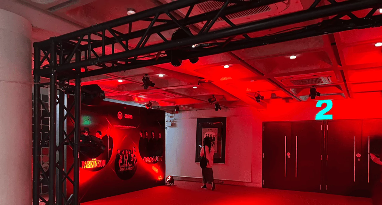 บรรยากาศทางเข้างานคอนเสิร์ต มีรูปภาพขนาดใหญ่ติดที่ผนัง แบคดรอปถ่ายรูปขนาดใหญ่และมีไฟสีแดง