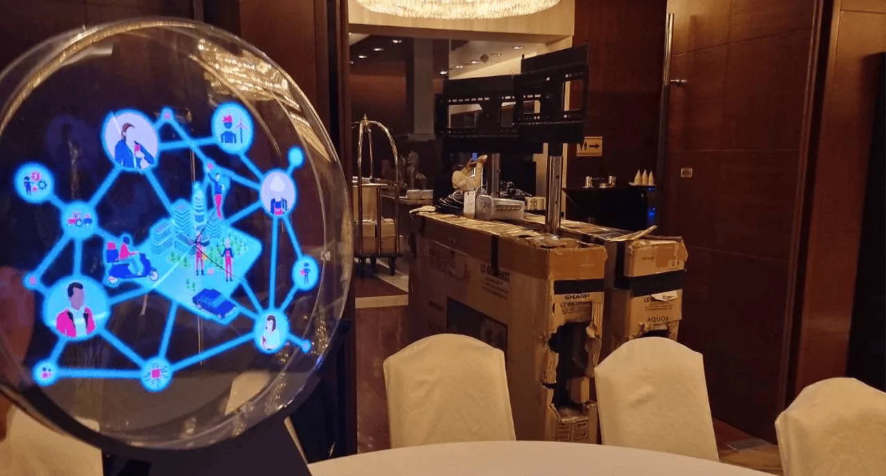 ที่นั่งสำหรับผู้มาสัมนา เก้าอี้ปูด้วยผ้าสีขาว โต๊ะกลมปูด้วยผ้าปูโต๊ะสีขาว ด้านหน้าเป็นเวที