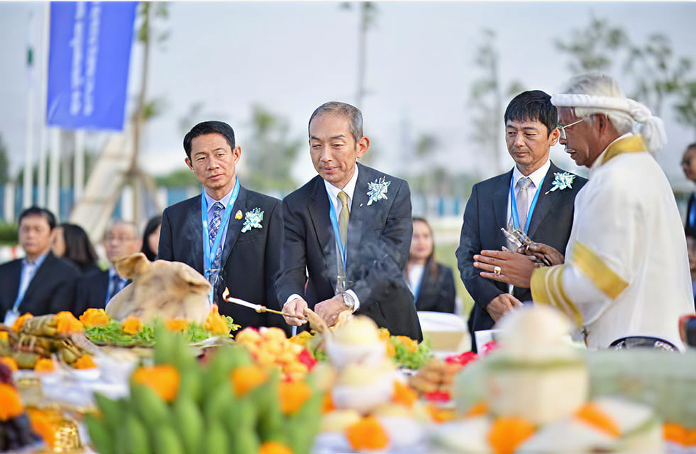 ผู้ชายใส่สูทถือเทียนที่จุดไว้แล้วด้านหน้ามีเครื่องเซ่นไหว้