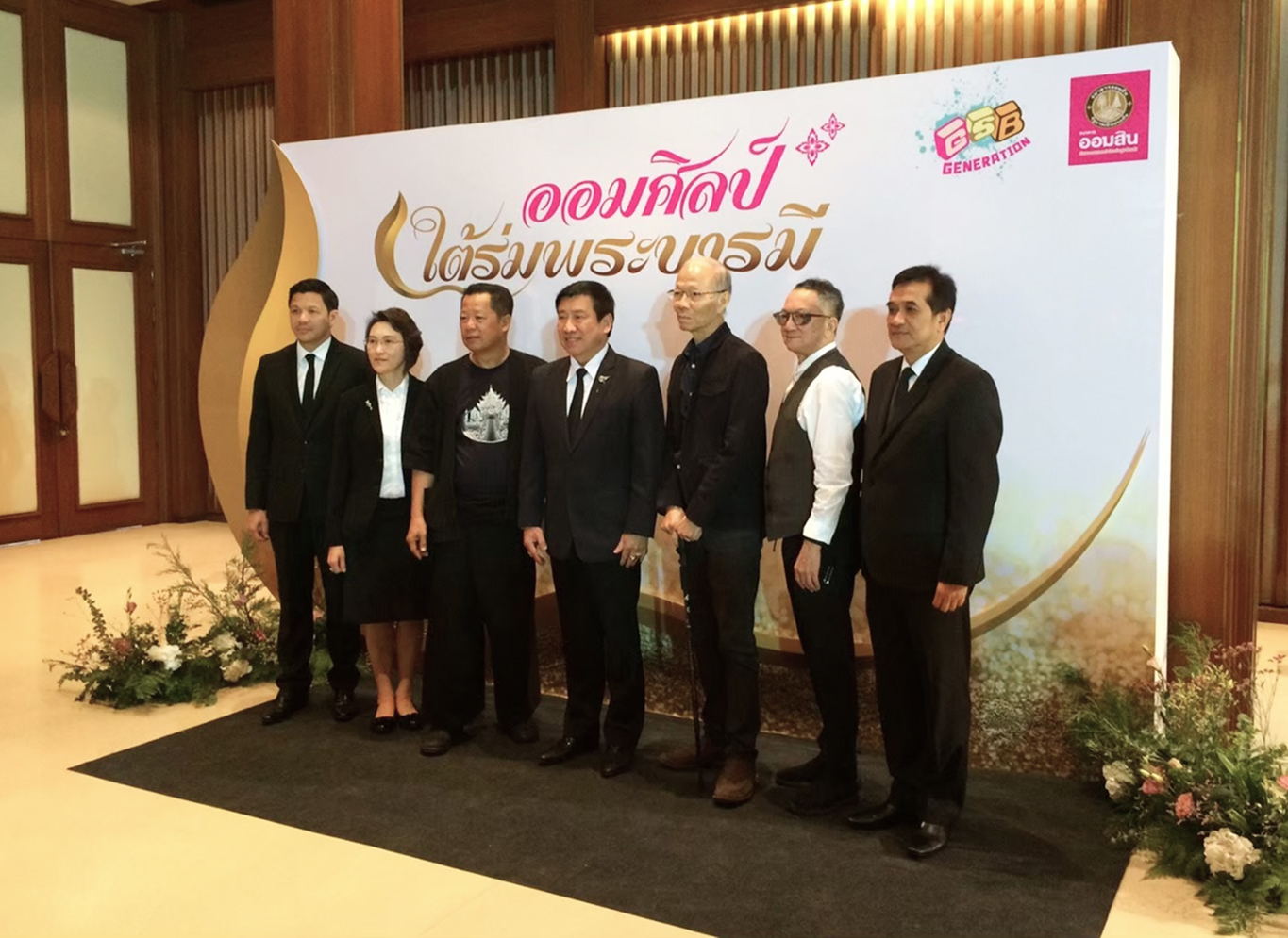 ผุ้ชายและผู้หญิงใส่สูทสีดำกำลังถ่ายรูปกับแบคดรอป