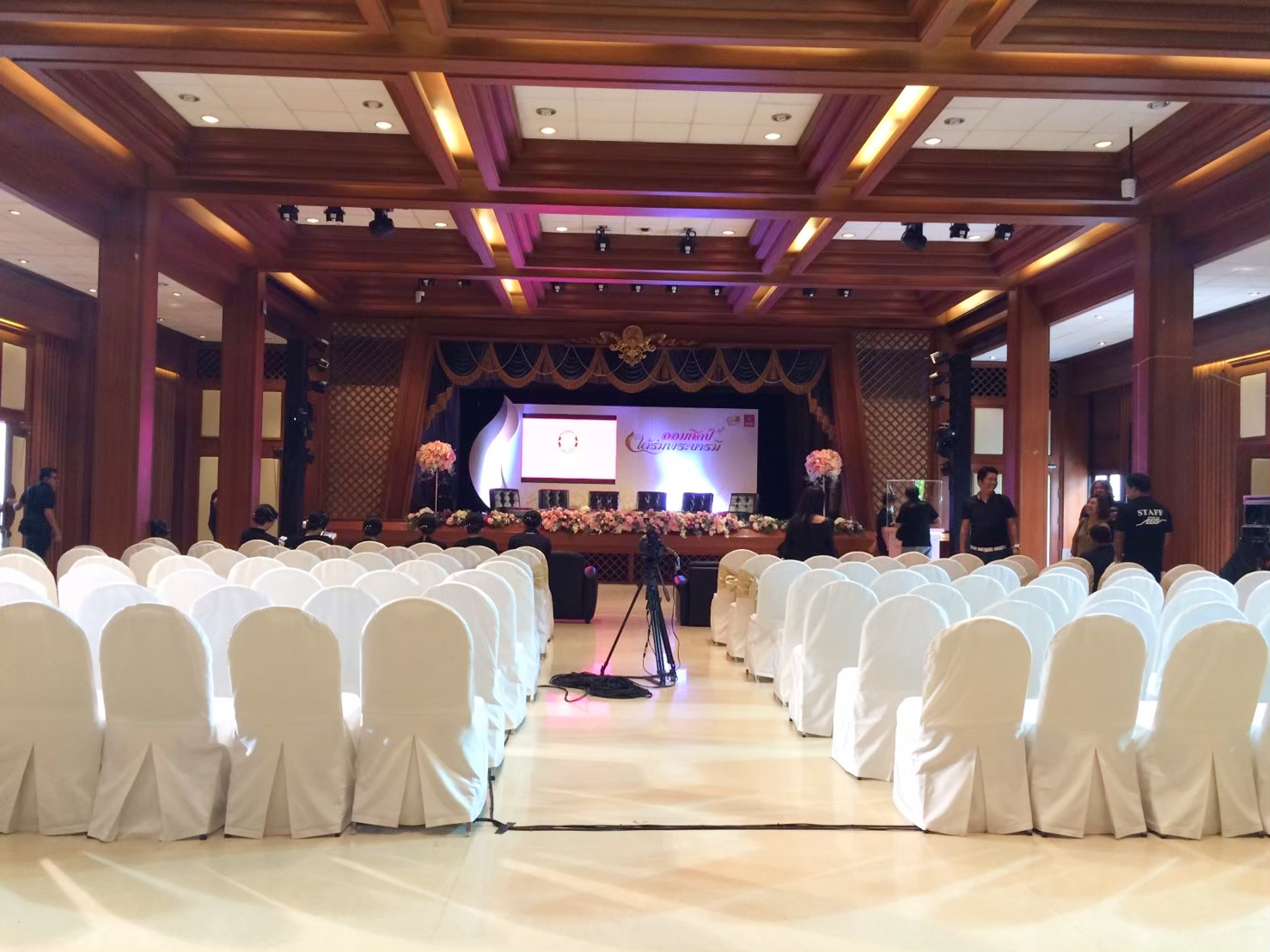 เก้าอี้สีขาววางเรียงกัน ด้านหน้าเป็นเวที มีจอโปรเจคเตอร์