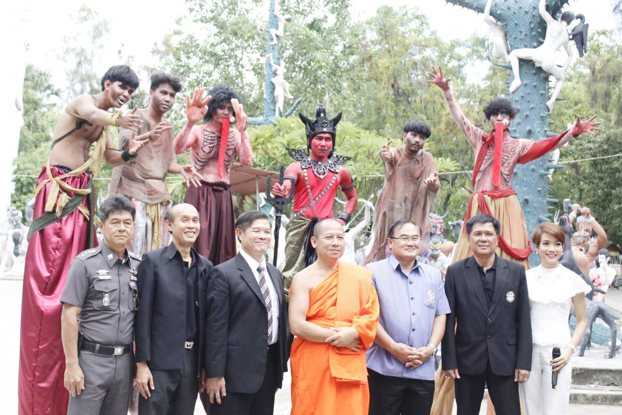 ผู้ชาย 6 คน และผู้หญิง กำลังยืนถ่ายรูปร่วมกับ ผู้ชายแต่งกายคล้ายเปรต ผี ยมทูต 5 คน