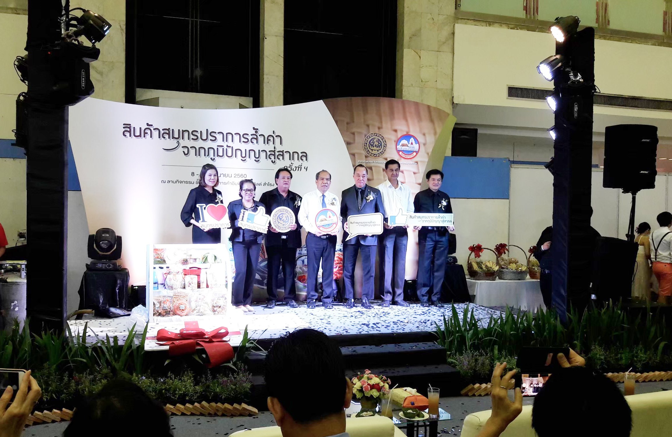 ผู้ชายผู้หญิงแต่งตัวทางการกำลังร่วมถ่ายภาพกันบนเวทีในงาน สินค้าจากภูมิปัญญา